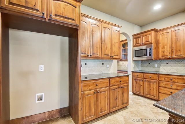 kitchen featuring decorative backsplash, stainless steel microwave, light tile patterned floors, and dark stone counters