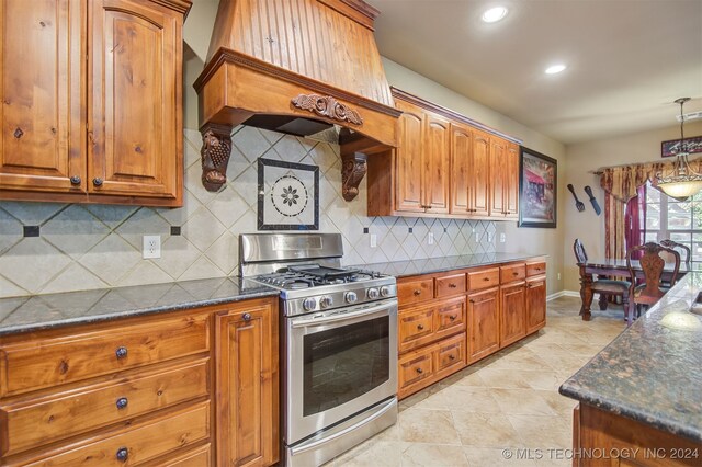 kitchen featuring stainless steel gas stove, decorative backsplash, decorative light fixtures, and dark stone countertops