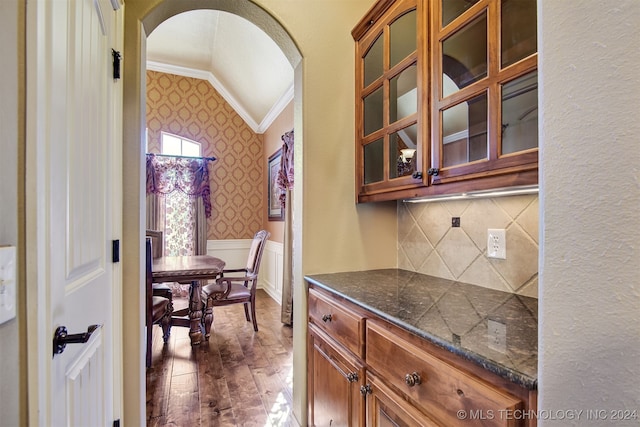 bar featuring vaulted ceiling, dark wood-type flooring, crown molding, dark stone countertops, and decorative backsplash