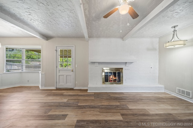 unfurnished living room featuring hardwood / wood-style flooring, beam ceiling, a brick fireplace, a textured ceiling, and ceiling fan