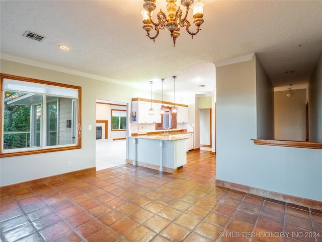 kitchen with sink, crown molding, pendant lighting, white cabinetry, and a textured ceiling