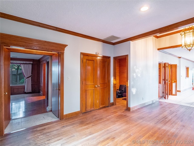 empty room with ornamental molding, a textured ceiling, and light wood-type flooring