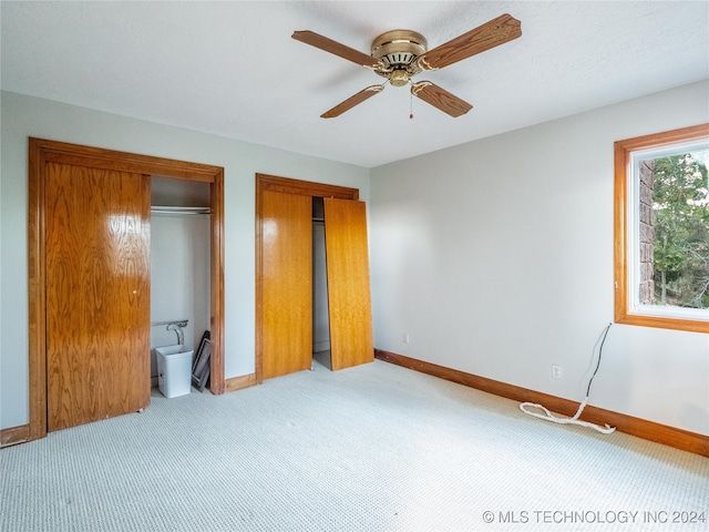 unfurnished bedroom with light carpet, ensuite bath, two closets, and ceiling fan