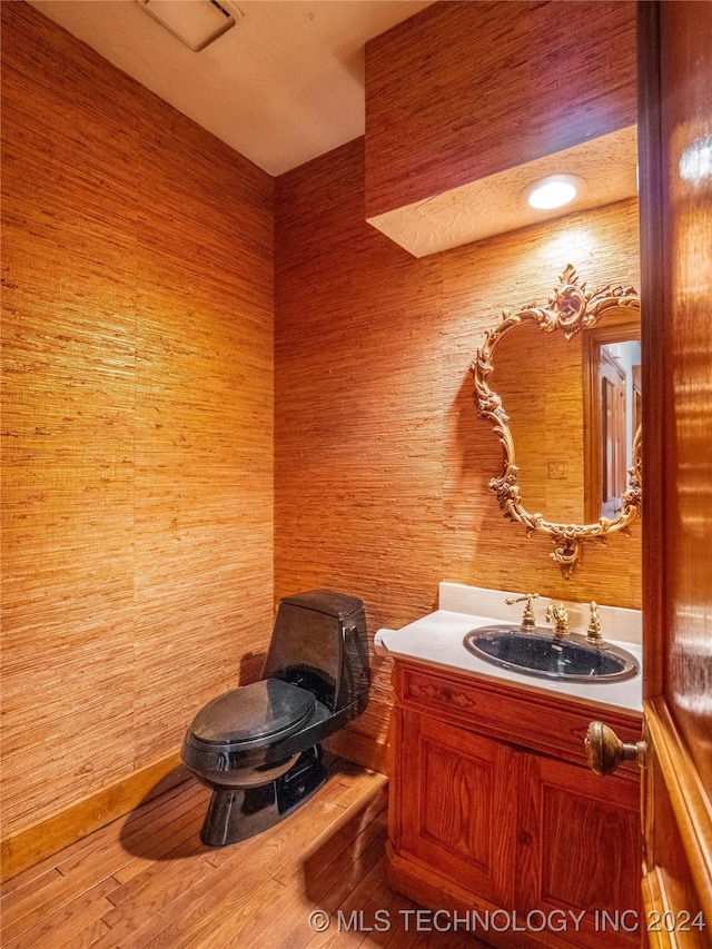 bathroom with vanity, wooden walls, wood-type flooring, and toilet