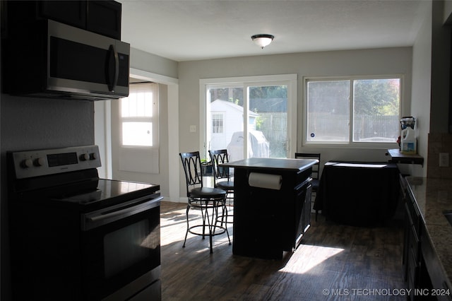 kitchen with dark wood-type flooring, appliances with stainless steel finishes, a center island, and a kitchen bar