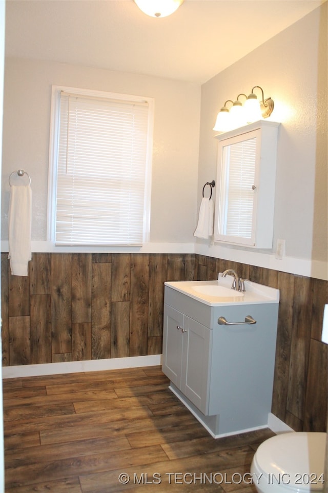 bathroom featuring vanity, toilet, wood-type flooring, and wooden walls