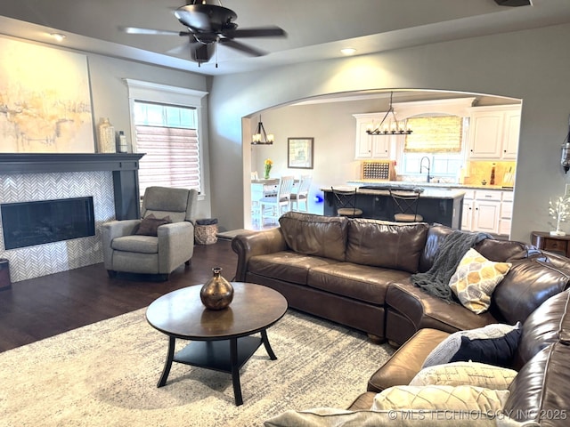 living room with hardwood / wood-style flooring, a tile fireplace, sink, and ceiling fan with notable chandelier