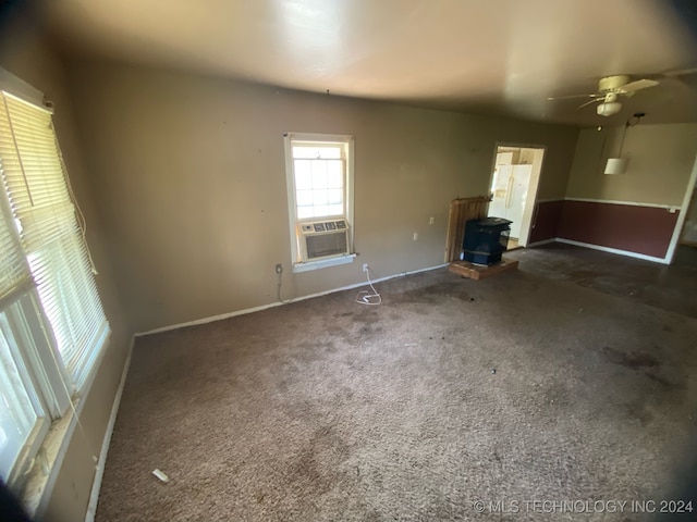 unfurnished living room featuring cooling unit, dark colored carpet, a wood stove, and ceiling fan