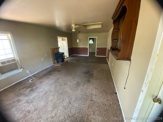 unfurnished living room featuring cooling unit, dark carpet, a skylight, and ceiling fan