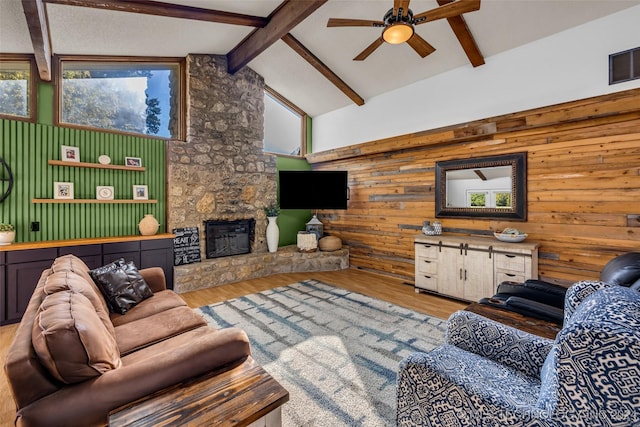 living room with beamed ceiling, a stone fireplace, high vaulted ceiling, and light hardwood / wood-style flooring