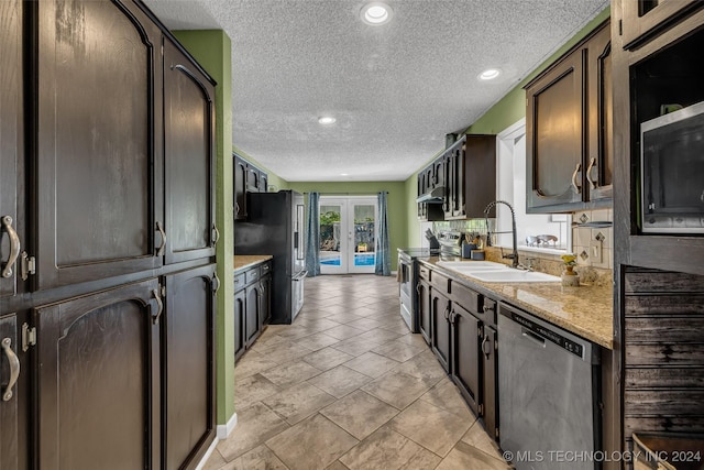 kitchen with sink, dark brown cabinetry, light stone counters, stainless steel appliances, and french doors