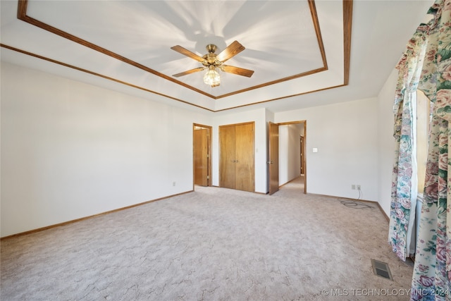 unfurnished bedroom featuring light carpet, a tray ceiling, and ceiling fan