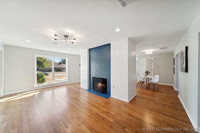 unfurnished living room with an inviting chandelier, a large fireplace, and light wood-type flooring