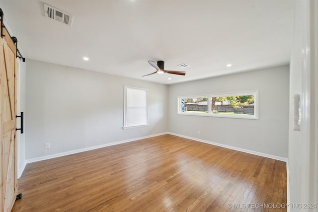 unfurnished room with a barn door, hardwood / wood-style flooring, and ceiling fan