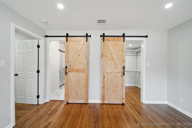 unfurnished bedroom with a closet, a walk in closet, hardwood / wood-style floors, and a barn door