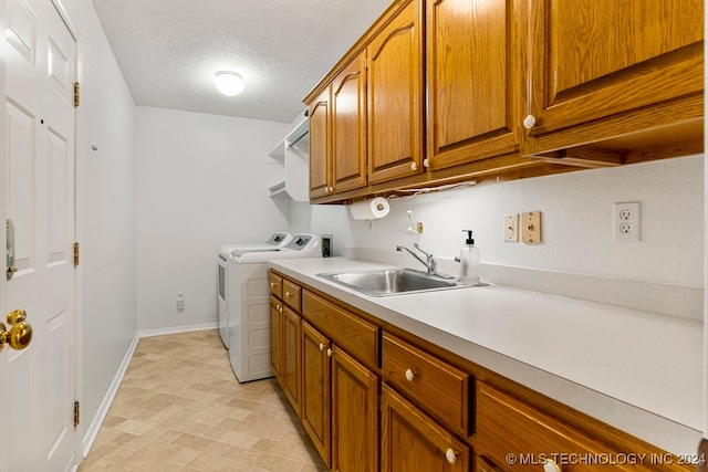 laundry area with a textured ceiling, cabinets, separate washer and dryer, and sink