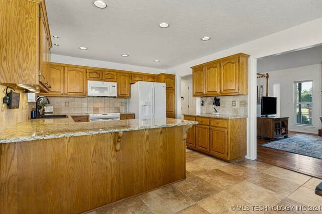 kitchen featuring sink, white appliances, kitchen peninsula, backsplash, and light stone countertops