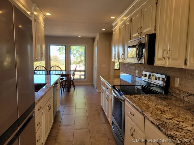 kitchen featuring light stone countertops, light tile patterned flooring, white cabinets, appliances with stainless steel finishes, and tasteful backsplash