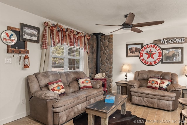 living room with ceiling fan, a wood stove, and light hardwood / wood-style flooring