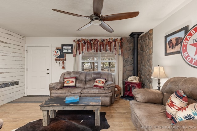 living room with light hardwood / wood-style floors, a wood stove, wooden walls, and ceiling fan