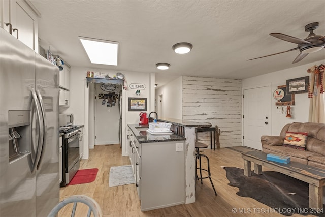 kitchen with appliances with stainless steel finishes, light wood-type flooring, a kitchen bar, a textured ceiling, and white cabinets