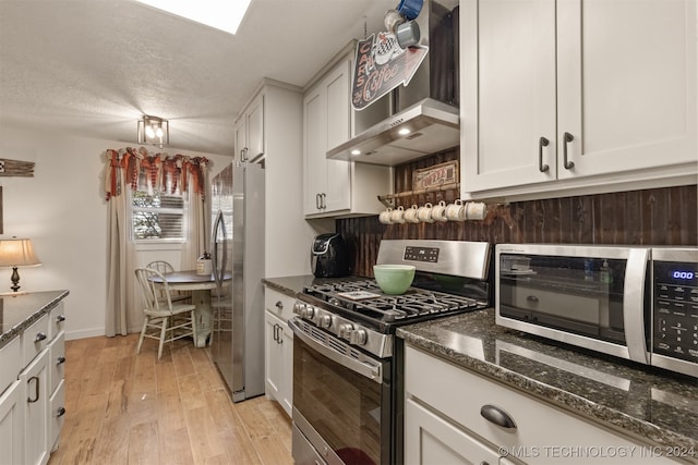 kitchen with appliances with stainless steel finishes, wall chimney range hood, light hardwood / wood-style flooring, and white cabinetry