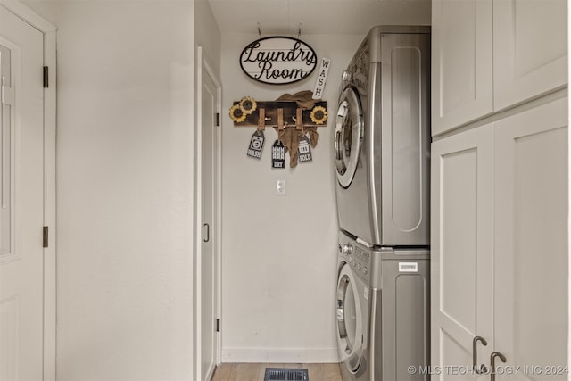 laundry room featuring stacked washer and dryer, light hardwood / wood-style floors, and cabinets