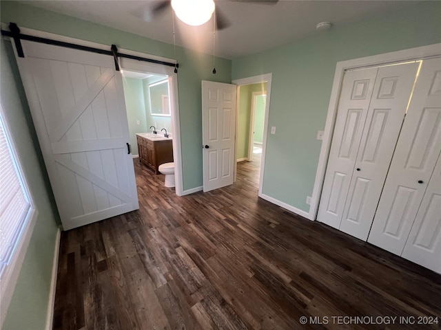 unfurnished bedroom featuring sink, dark wood-type flooring, ensuite bathroom, a barn door, and a closet