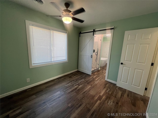 unfurnished bedroom featuring ceiling fan, a barn door, dark hardwood / wood-style flooring, and ensuite bath