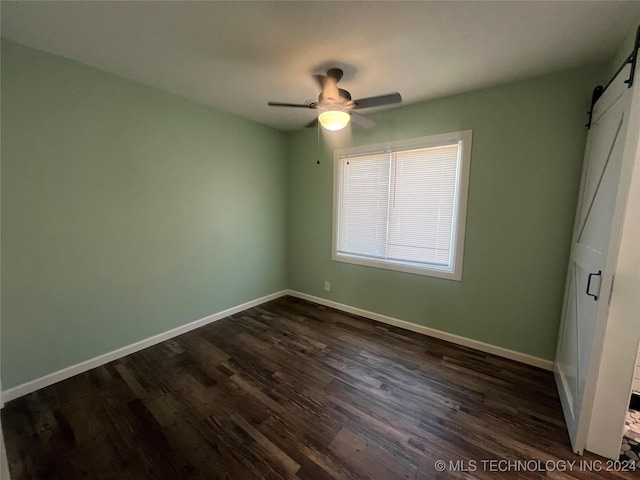 unfurnished bedroom with dark hardwood / wood-style floors, a barn door, and ceiling fan