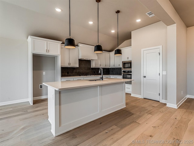 kitchen with custom range hood, vaulted ceiling, built in microwave, a center island with sink, and hanging light fixtures