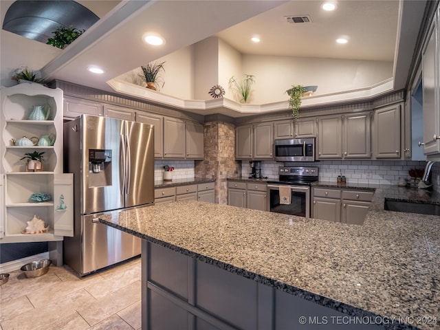 kitchen with gray cabinetry, kitchen peninsula, stainless steel appliances, dark stone counters, and decorative backsplash