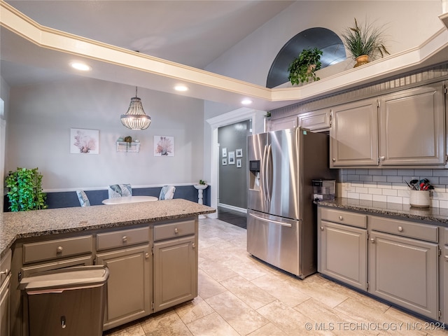 kitchen with backsplash, dark stone counters, vaulted ceiling, pendant lighting, and stainless steel refrigerator with ice dispenser