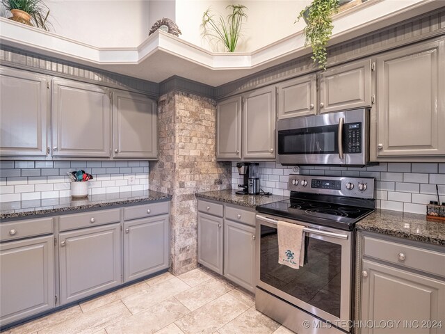 kitchen with gray cabinetry, stainless steel appliances, and dark stone counters