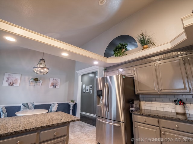 kitchen with backsplash, lofted ceiling, pendant lighting, dark stone counters, and stainless steel fridge with ice dispenser