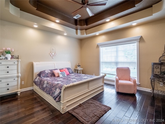 bedroom with ceiling fan, a tray ceiling, and dark hardwood / wood-style floors