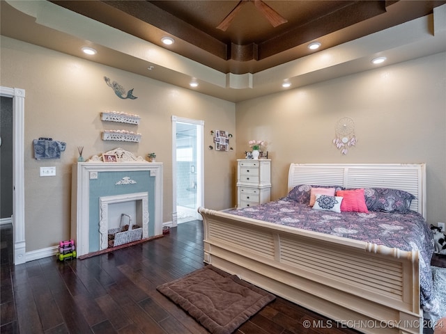 bedroom featuring dark wood-type flooring, a tray ceiling, connected bathroom, and ceiling fan