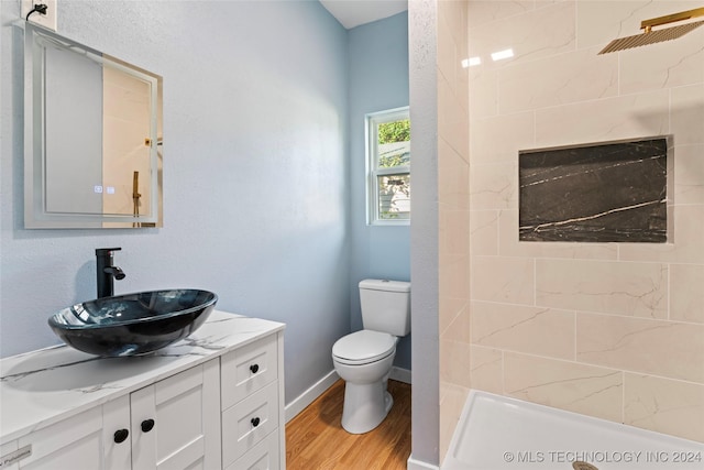 bathroom featuring hardwood / wood-style flooring, vanity, toilet, and a tile shower