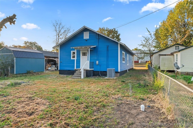 rear view of house featuring an outbuilding, a yard, and central AC