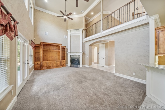 unfurnished living room featuring crown molding, a towering ceiling, light colored carpet, and ceiling fan