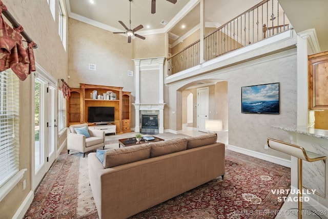 living room with ornamental molding, a towering ceiling, ceiling fan, and a fireplace