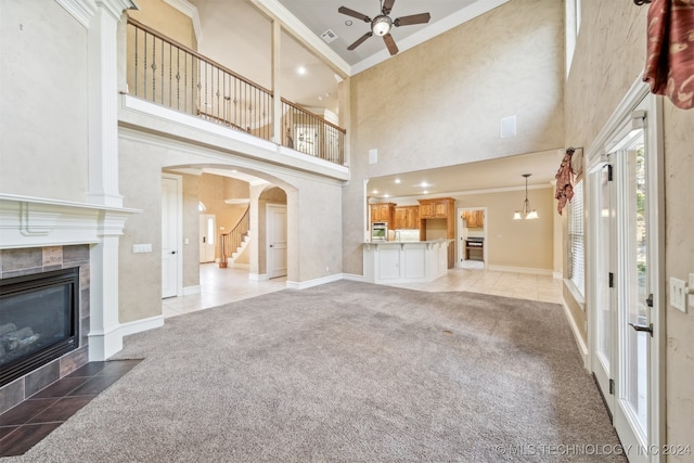 unfurnished living room with a high ceiling, ornamental molding, light colored carpet, a fireplace, and ceiling fan