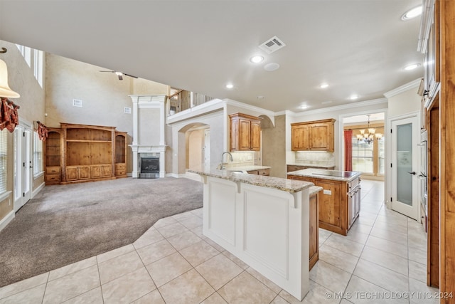 kitchen featuring sink, kitchen peninsula, a tile fireplace, light stone counters, and light colored carpet