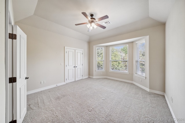 unfurnished bedroom with ceiling fan, a tray ceiling, vaulted ceiling, and carpet