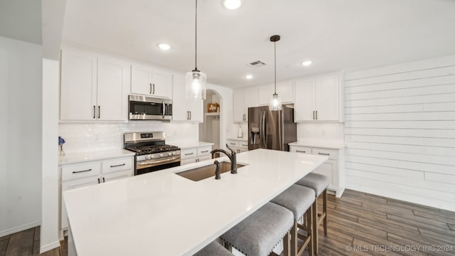 kitchen with appliances with stainless steel finishes, sink, pendant lighting, dark hardwood / wood-style floors, and a kitchen island with sink