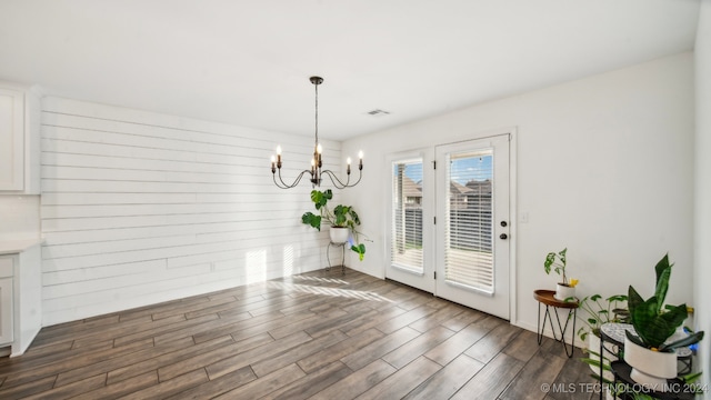 dining space with an inviting chandelier, wooden walls, and dark wood-type flooring