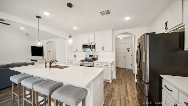 kitchen featuring dark wood-type flooring, stainless steel appliances, a center island with sink, sink, and white cabinetry