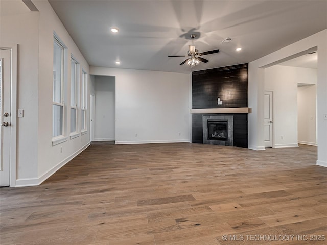 unfurnished living room featuring a tile fireplace, ceiling fan, and light hardwood / wood-style flooring