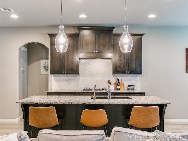 kitchen featuring dark brown cabinetry, decorative light fixtures, tasteful backsplash, and an island with sink