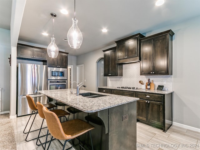 kitchen with dark brown cabinets, a kitchen island with sink, sink, pendant lighting, and stainless steel appliances